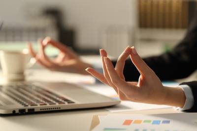 Nahaufnahme einer Frau, die in einer Yoga-Pose an ihrem Schreibtisch im Büro sitzt